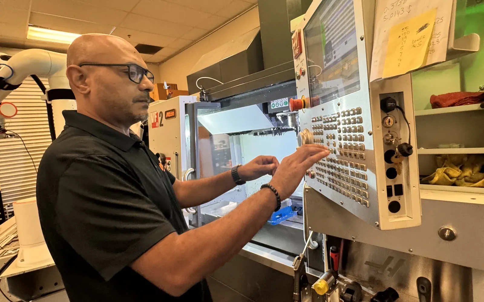 Michael Nessim running a Haas CNC mill from its control panel, with a cobot arm beside the machine